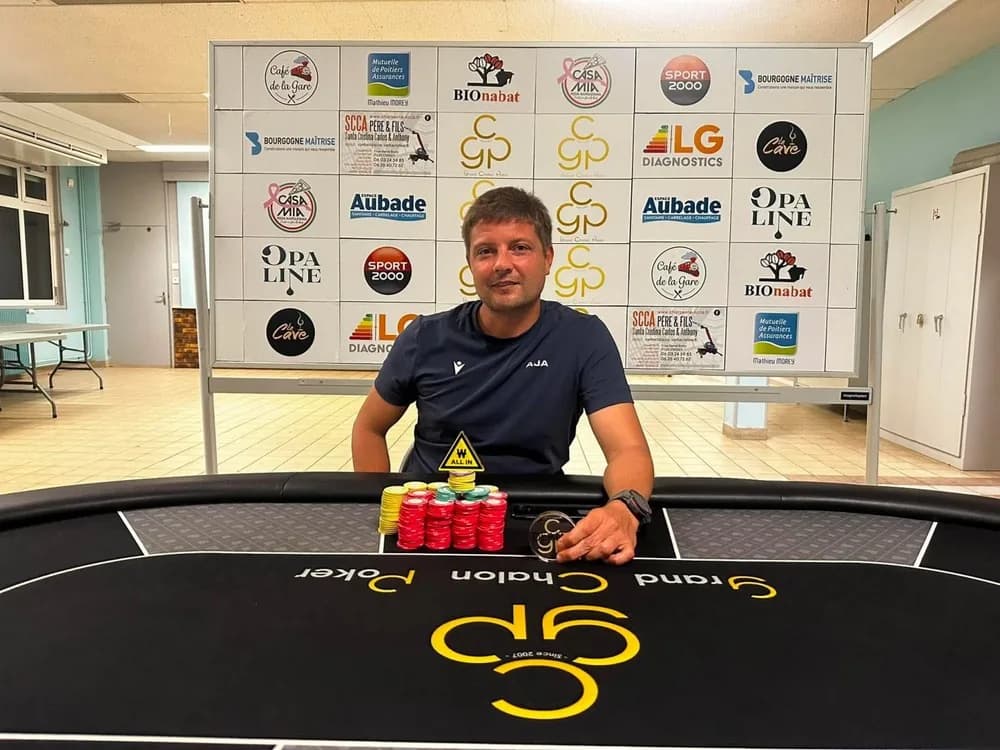 Un joueur derrière une table du Grand Chalon Poker, devant le panneau des partenaires du club